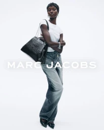 Model wearing a white t-shirt and grey jeans carrying a black handbag against white