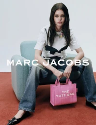 Model seated in an armchair holding a pink tote bag for the Marc Jacobs Spring 2025 campaign