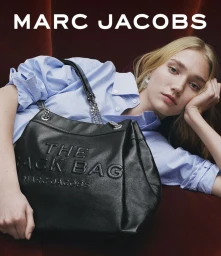 Model in blue pinstripe shirt holding a black leather tote bag against dark red upholstery