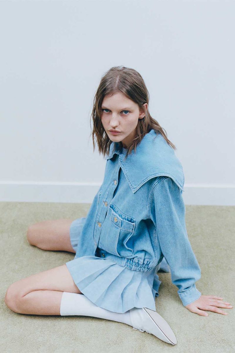 Model Nadine Kirilova wearing denim jacket and pleated skirt seated on floor for Claudie Pierlot campaign