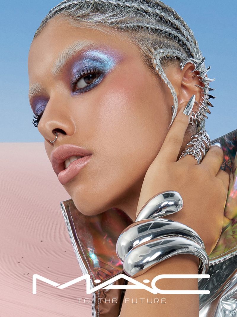 Close-up studio shot of a woman with silver braided hair, dramatic eye makeup, and a silver snake bracelet, in a fashion-forward beauty ad.