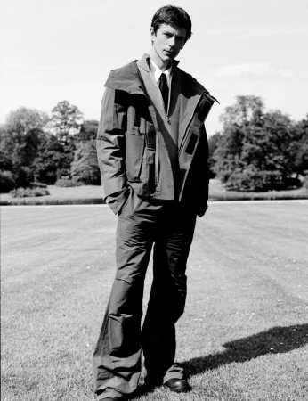 Model Jeremy Young wearing a utility jacket and trousers standing outdoors on a lawn for Berner Kühl Spring Summer 2025.