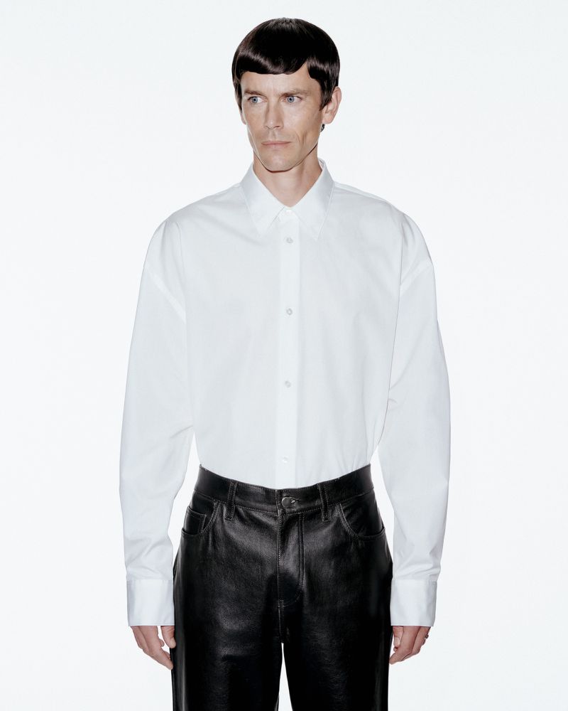 Model Jeremy Young wearing a white button-down shirt and black trousers against a plain white background for Berner Kühl