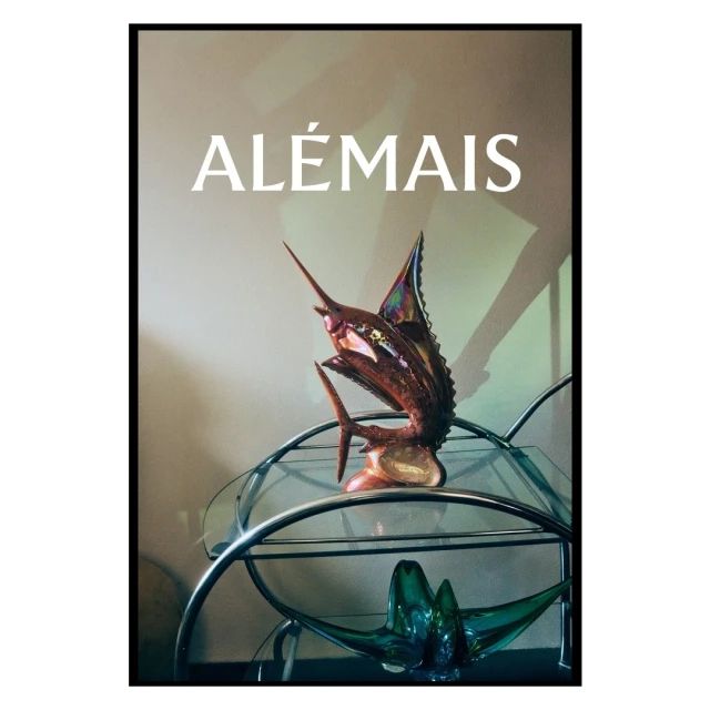 Artwork featuring a copper sailfish sculpture on a glass and chrome cart, set against a neutral wall with the text 'ALÉMAIS' above.