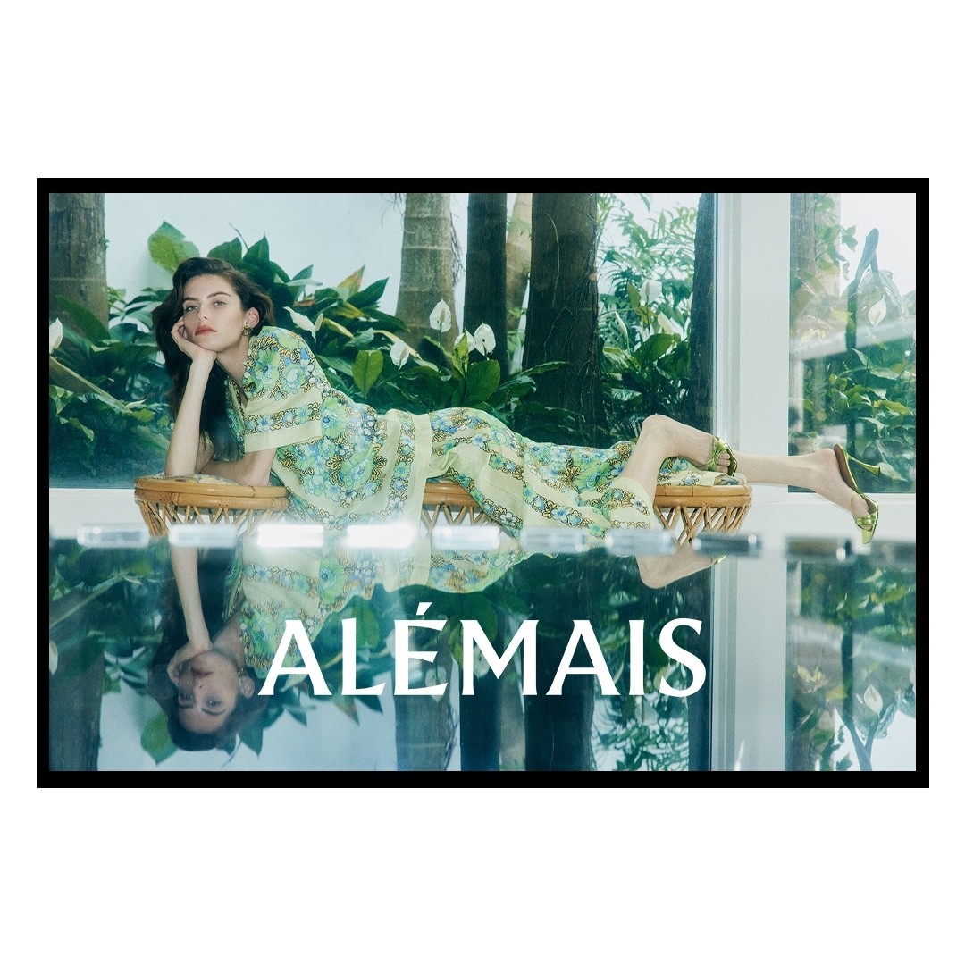 Woman in patterned green dress reclining on a rattan bench with lush tropical foliage in the background and a reflected foreground overlay