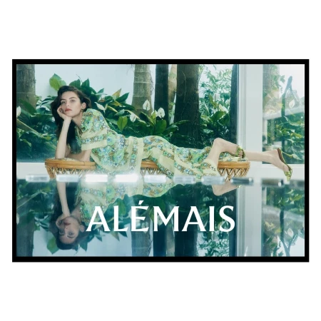 Woman in patterned green dress reclining on a rattan bench with lush tropical foliage in the background and a reflected foreground overlay