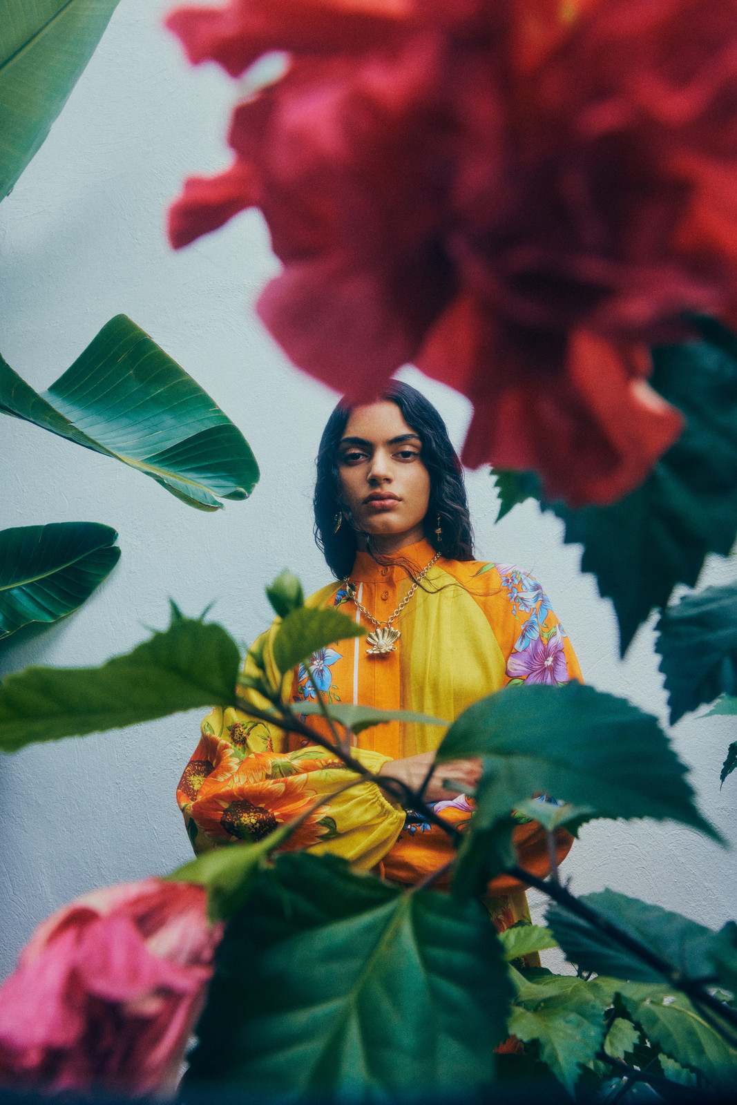 Portrait of an adult woman with floral-patterned sleeves, tropical leaves and bright pink flowers framing the shot.