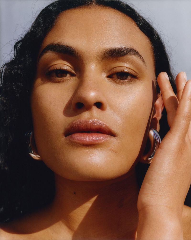 Close-up portrait of a radiant woman with curly hair, showcasing glowing skin, accented by silver hoop earrings, and subtle shadows.