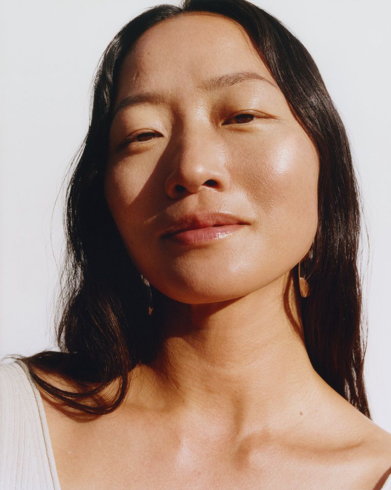 Close-up portrait of an Asian woman with dark hair, smooth skin, and natural makeup, against a white background with soft, diffused lighting.