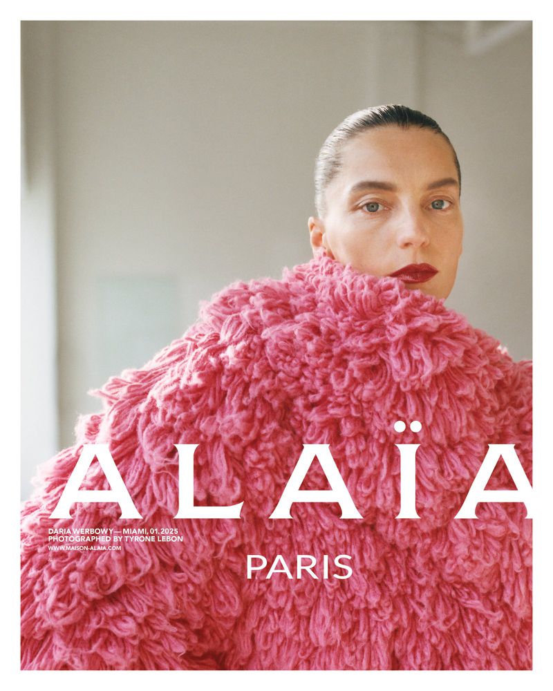 Fashion editorial shot: Woman in pink textured coat, bold red lipstick against a blurred background, featuring Alaïa Paris logo.