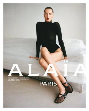 Model Daria Werbowy seated on a white plastic-wrapped sofa wearing a black bodysuit and mesh flats for Alaia