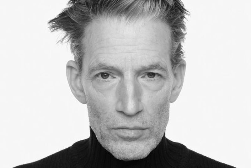 Headshot of adult male in black turtleneck sweater, black and white image on white background. Focused expression, eye-level framing.