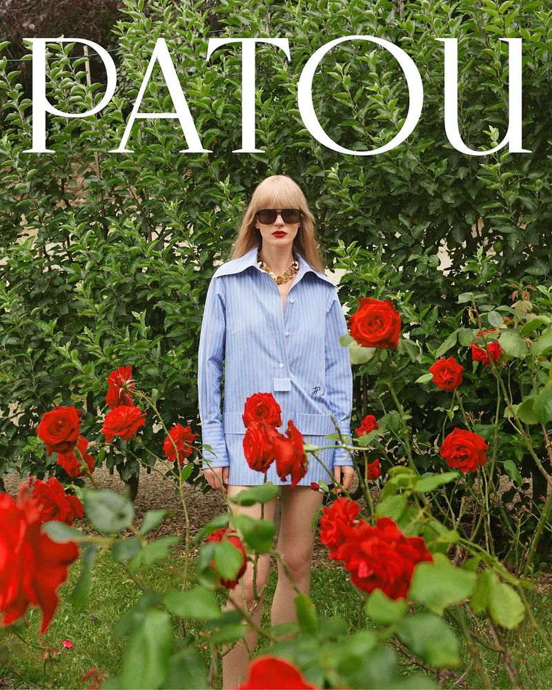An adult female model poses in a blue pinstripe outfit and sunglasses in a rose garden for a fashion editorial with Patou text overlay.