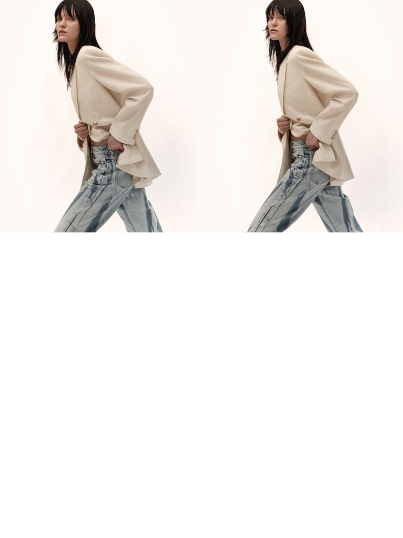 Two fashionable women wearing blazers and jeans walk in a light, bright photo studio, showcasing current trends and styles.