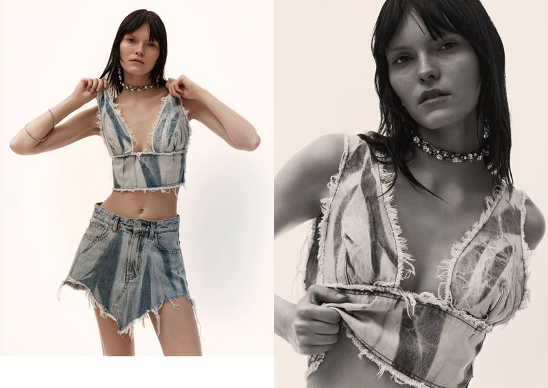 A fair-skinned woman poses indoors, wearing a distressed denim crop top and skirt, complemented by a choker necklace and silver bracelets.