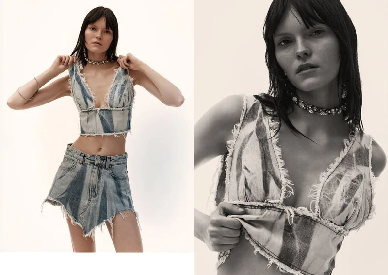 A fair-skinned woman poses indoors, wearing a distressed denim crop top and skirt, complemented by a choker necklace and silver bracelets.