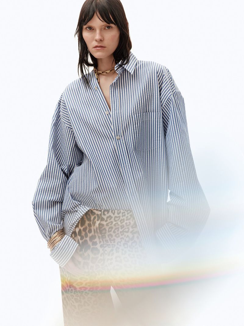 Model wearing oversized blue striped button down shirt and leopard print pants against white backdrop