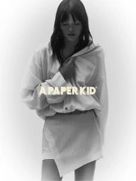 Model with dark hair wearing an oversized striped shirt and skirt against a seamless white background