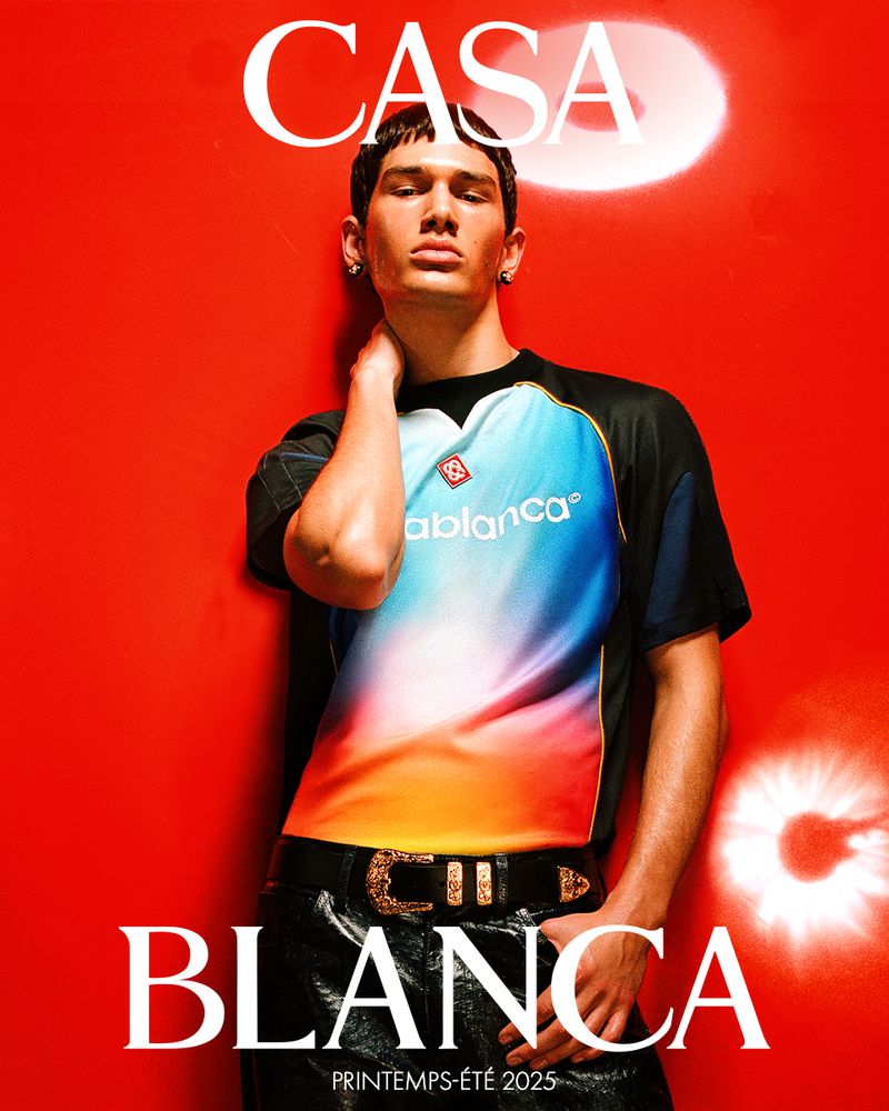 A male model poses against a red wall in a Casablanca T-shirt with black pants and belt, advertising the brand's Printemps-Été 2025 collection.