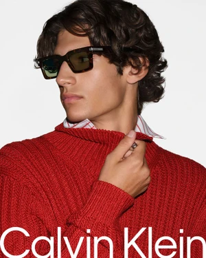 Close-up portrait of a male model wearing tortoiseshell sunglasses and a red ribbed knit sweater against a white background