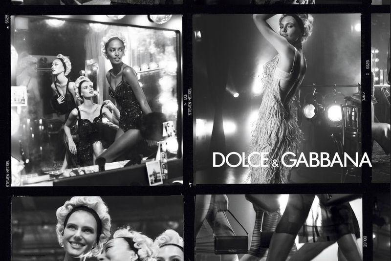 Black and white fashion campaign ad featuring models in vintage-inspired outfits, posing in a backstage dressing room setting under bright lights.