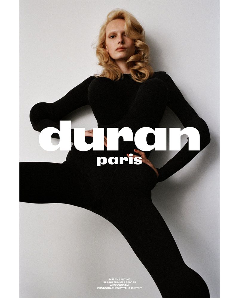 Fashion portrait of a blonde woman wearing a black bodysuit against a white background with graphic text overlay, shot in studio.
