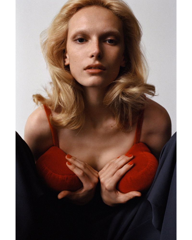 Blonde woman in red bra poses against a white backdrop with black pants; studio lighting and a medium shot show off her fair skin.
