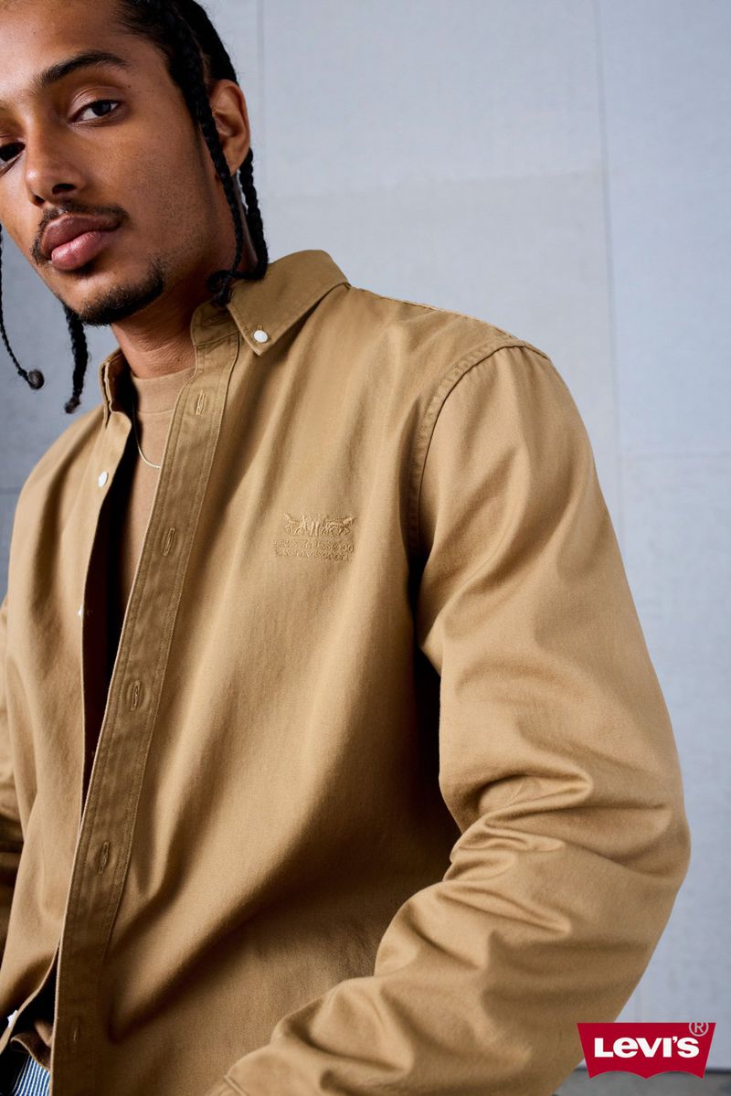Close-up of a male model in a tan button-down shirt, showcasing the garment's fit and design against a neutral backdrop. 