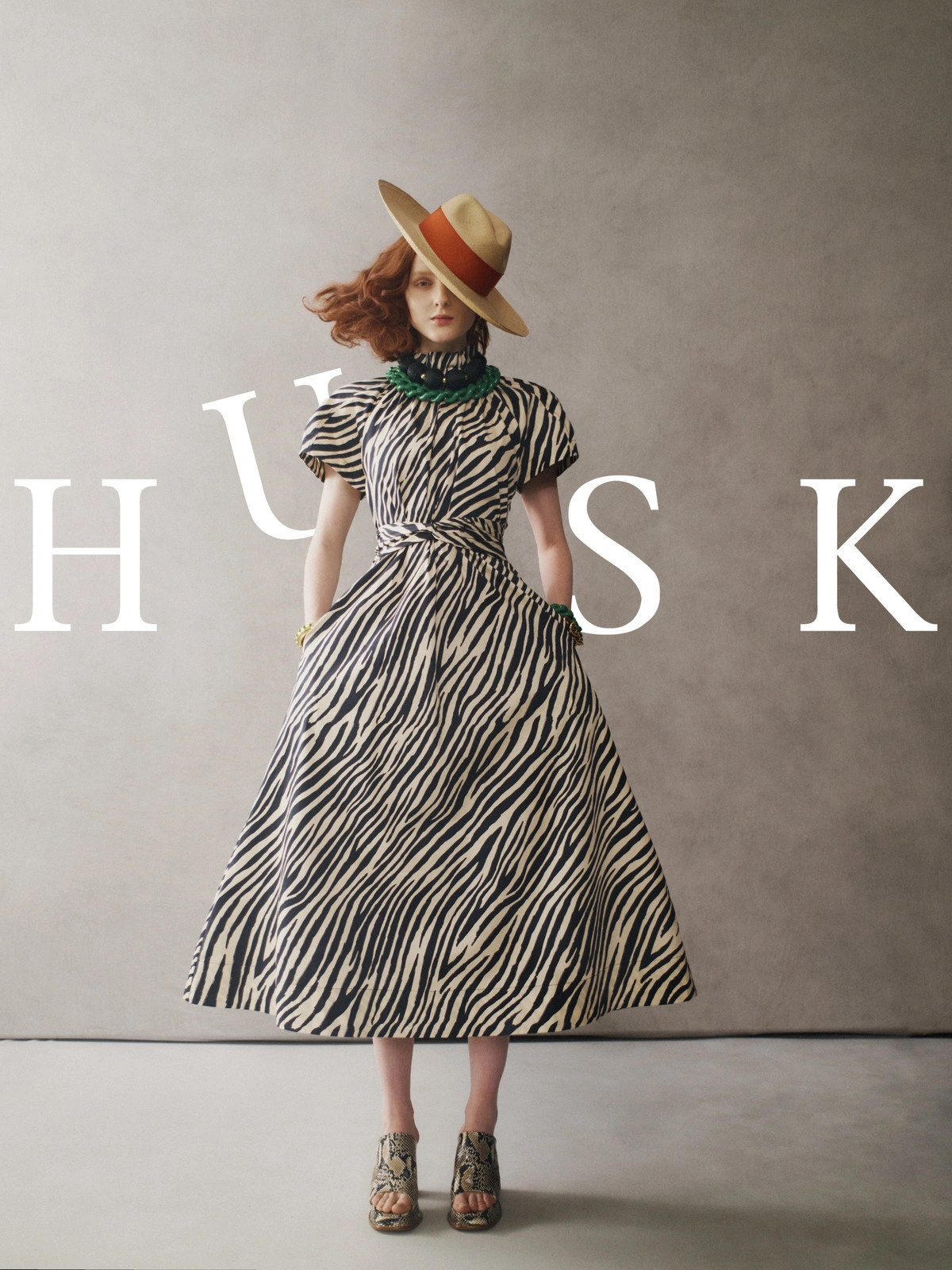 Model wearing a zebra print dress and wide-brim hat against a neutral textured studio background with overlaid HUSK typography