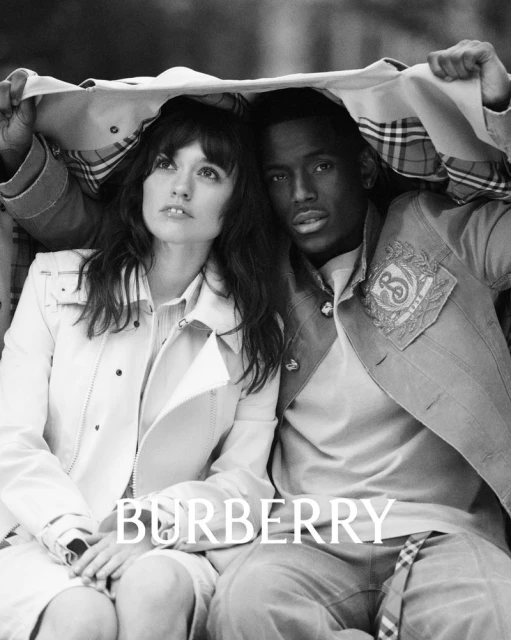 A stylish black-and-white portrait of two adults under a beige jacket, with the Burberry logo overlaid, capturing a timeless fashion moment.