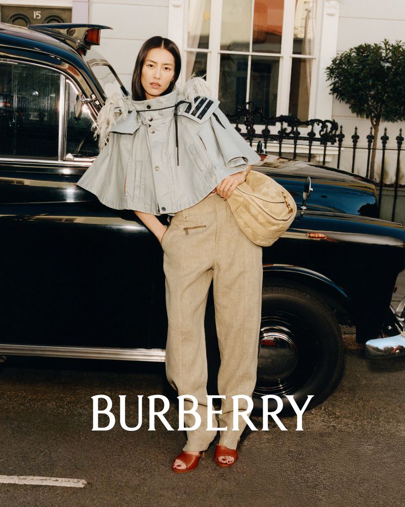 Fashion shot featuring an Asian woman in stylish cape and trousers, next to a black taxi cab, with the brand BURBERRY visible.