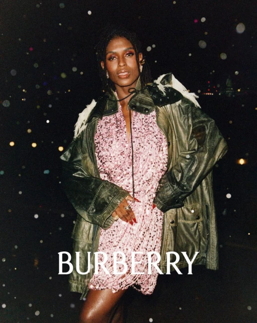 Adult female model showcases a pink fringe dress with a leather jacket against a bokeh-lit cityscape at night in a Burberry advertisement.