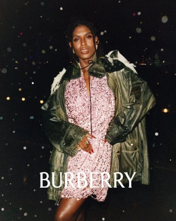 Adult female model showcases a pink fringe dress with a leather jacket against a bokeh-lit cityscape at night in a Burberry advertisement.