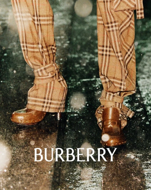 Person wearing Burberry plaid pants and brown leather shoes standing on a wet, reflective surface with the Burberry logo visible.