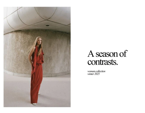 Indoor fashion shot of a blond woman in a red dress. She is standing in front of a light-stone wall in a minimalist, modern building.