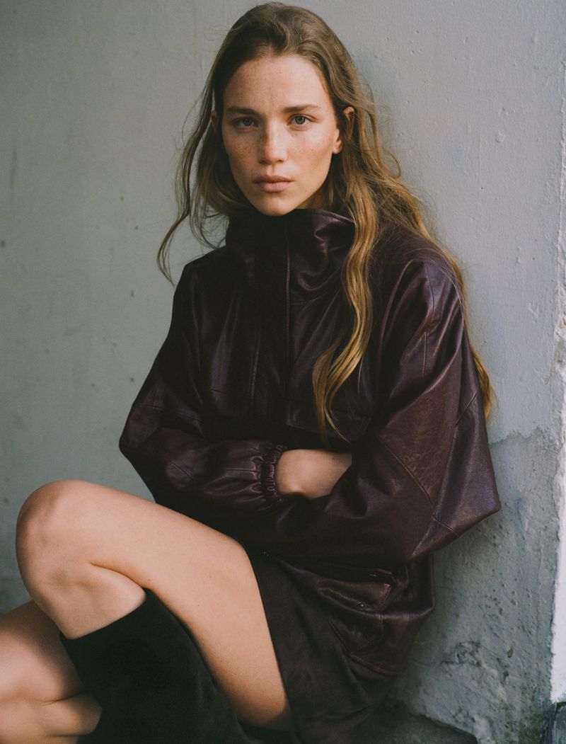 Model wearing a dark plum leather jacket seated against a plain neutral wall for Zara Woman Winter 2025 campaign.