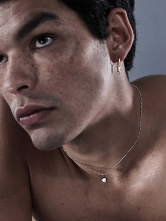 Close-up portrait of a man wearing delicate gold jewelry including earrings and a pendant necklace for Sarah & Sebastian.
