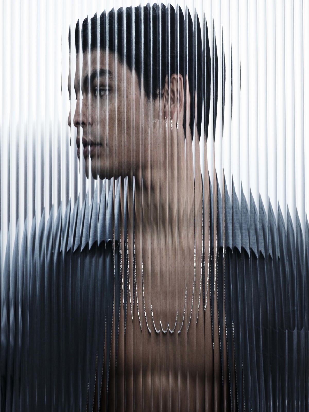 Stylish portrait of a male model behind textured glass, showcasing contemporary fashion, light skin, and clean studio aesthetic.