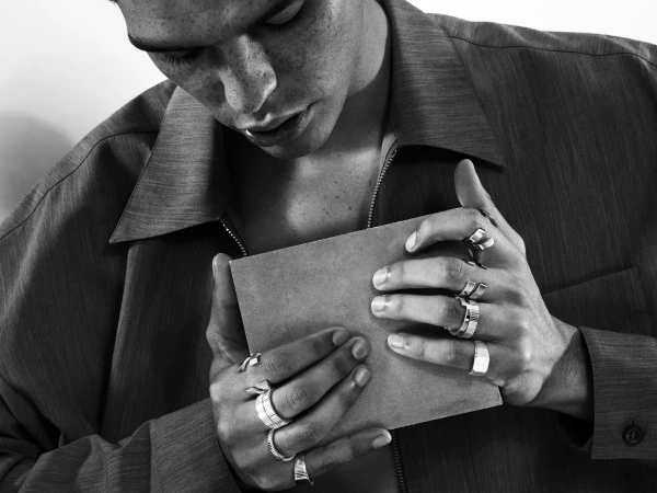 Close-up of a man wearing multiple silver rings on both hands while holding a small square object