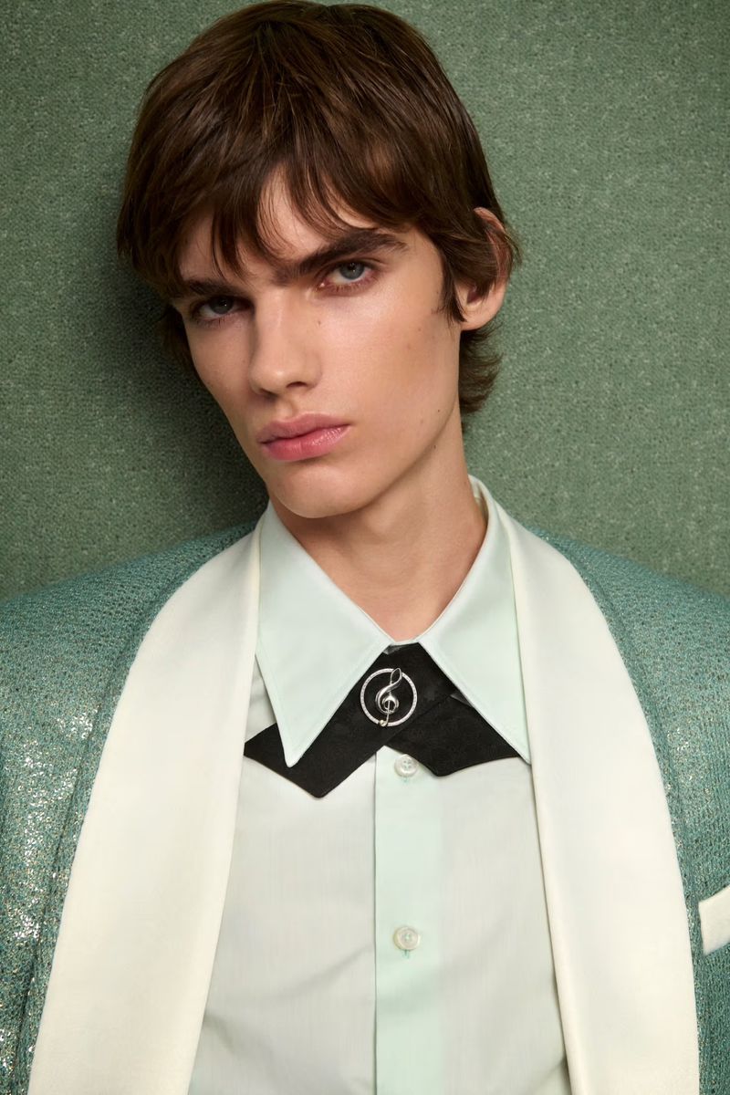 Portrait of a young adult male wearing a mint green shirt and a shimmering green blazer in a close-up studio shot.