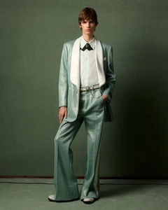 Full-length portrait of a male model wearing a light teal suit and white shirt against a textured green studio backdrop.