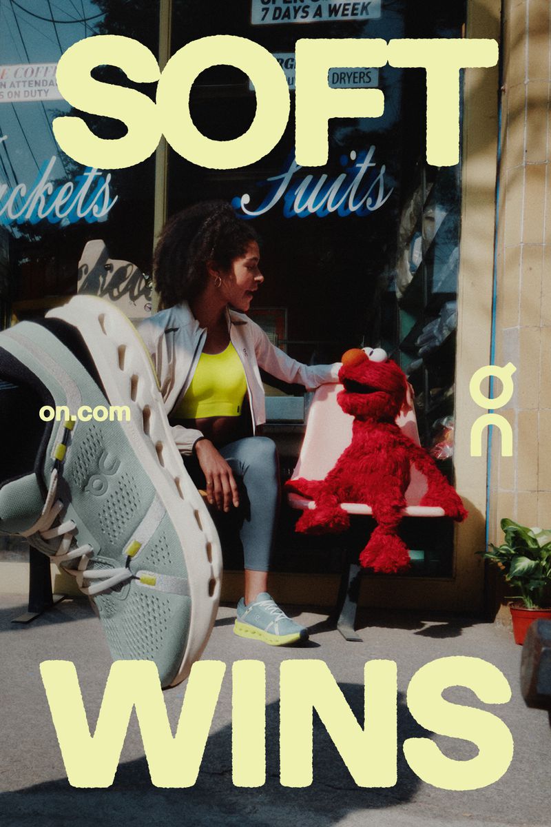 Outdoor advertising features sneakers, a woman, and Elmo at laundromat, showcasing a blend of fashion and whimsical character.