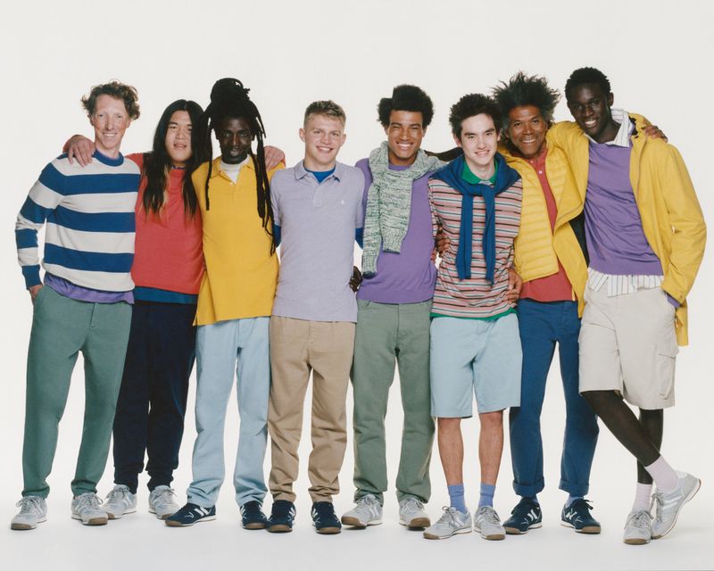 Group portrait of eight diverse young men standing together in casual wear against a white background, smiling and friendly.