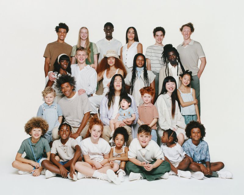 Diverse group of adults and children smiling and posing together in a light and airy setting, showcasing a range of ages and ethnicities.