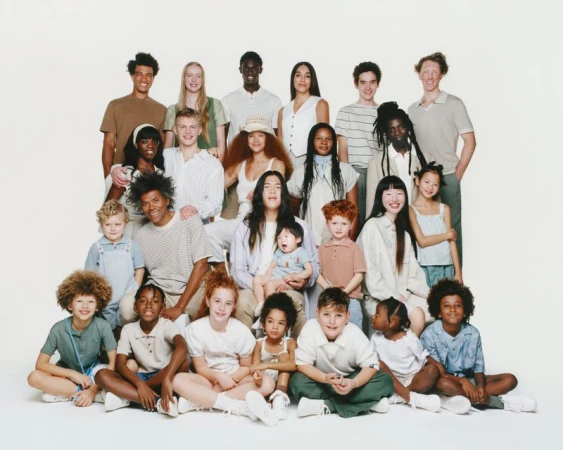 Diverse group of adults and children smiling and posing together in a light and airy setting, showcasing a range of ages and ethnicities.