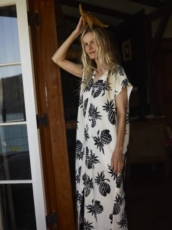 Elegant adult female in pineapple-print dress poses in doorway with starfish on head, bathed in natural light.