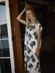 Blonde woman in a white dress with black pineapple prints holding a starfish on her head near open wooden doors