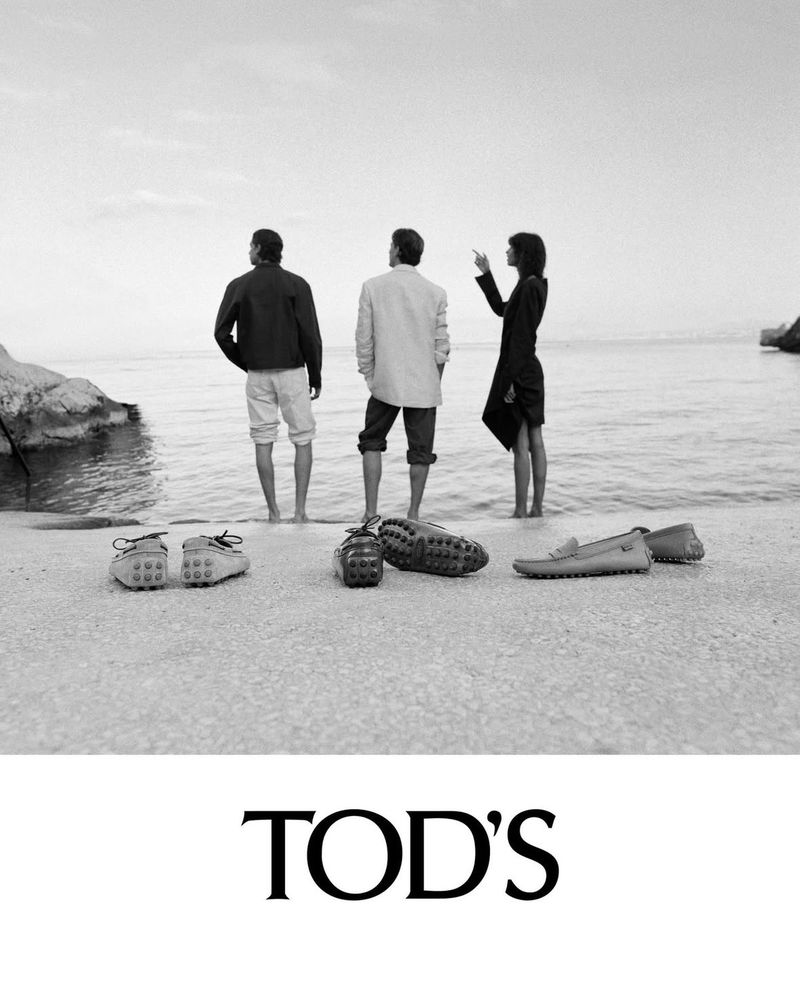 Tod's footwear displayed on a beach with two men and a woman standing by the ocean, black and white, fashion advertising campaign.