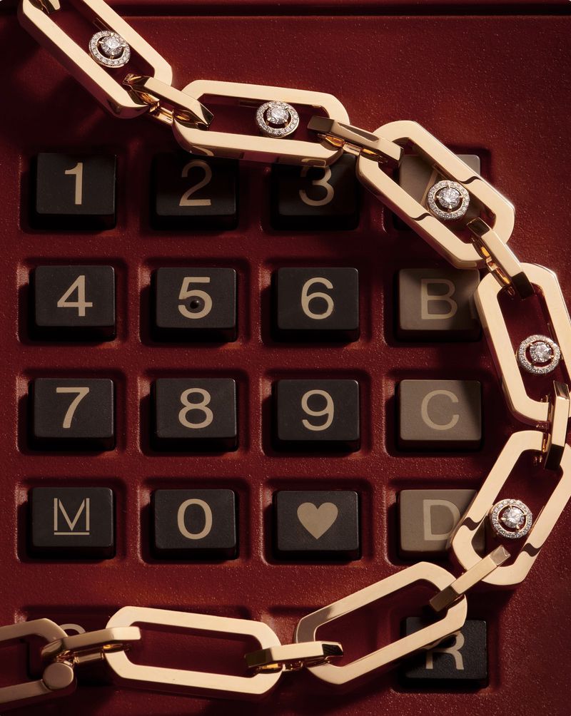 Close-up of a gold chain necklace with diamond accents draped over a dark red calculator with black buttons and white numerals.