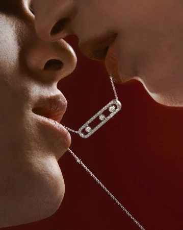 Close-up of two people holding a diamond necklace in their mouths, set against a red backdrop for a luxury jewelry advertisement.